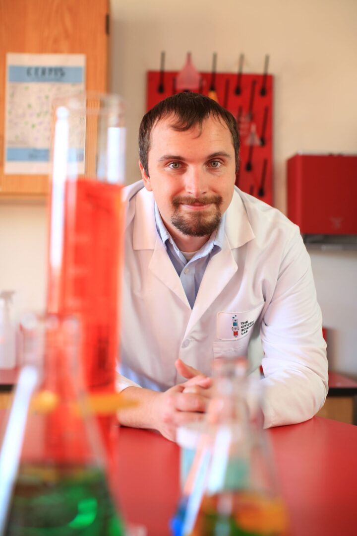 A man in lab coat sitting at table with red objects.