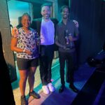 Three People Standing In A Room With Some Drinks.