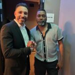 Two Men Standing Next To Each Other Holding A Pen.