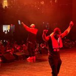 Two Men Are Dancing On A Stage With People Watching.